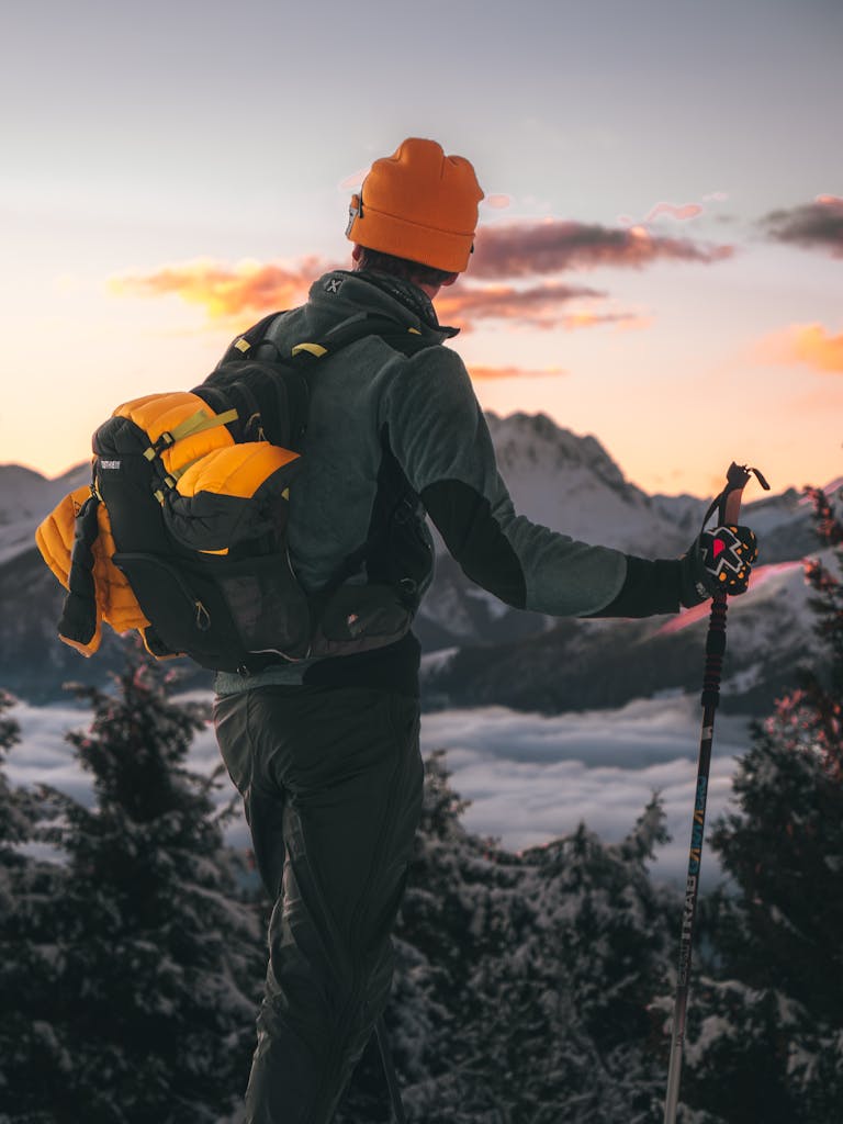 Hiker with trekking poles overlooks stunning mountain sunset, embodying adventure and tranquility.